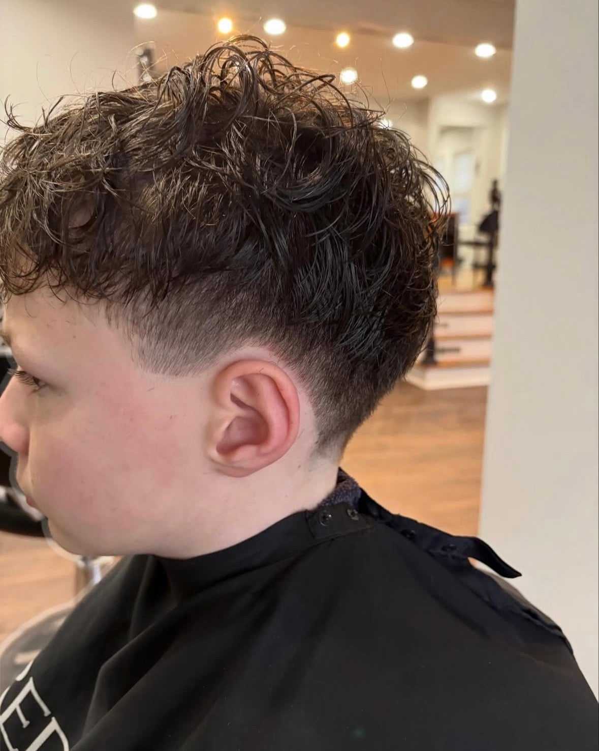 Young person with a fresh, curly haircut in a modern salon setting.