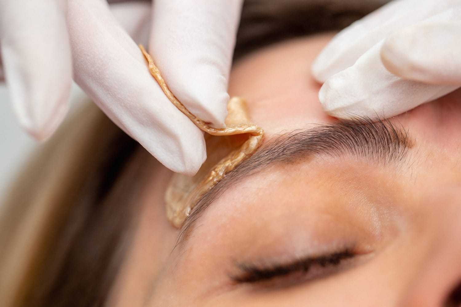 Waxing a person's eyebrow with gloves for hair removal.