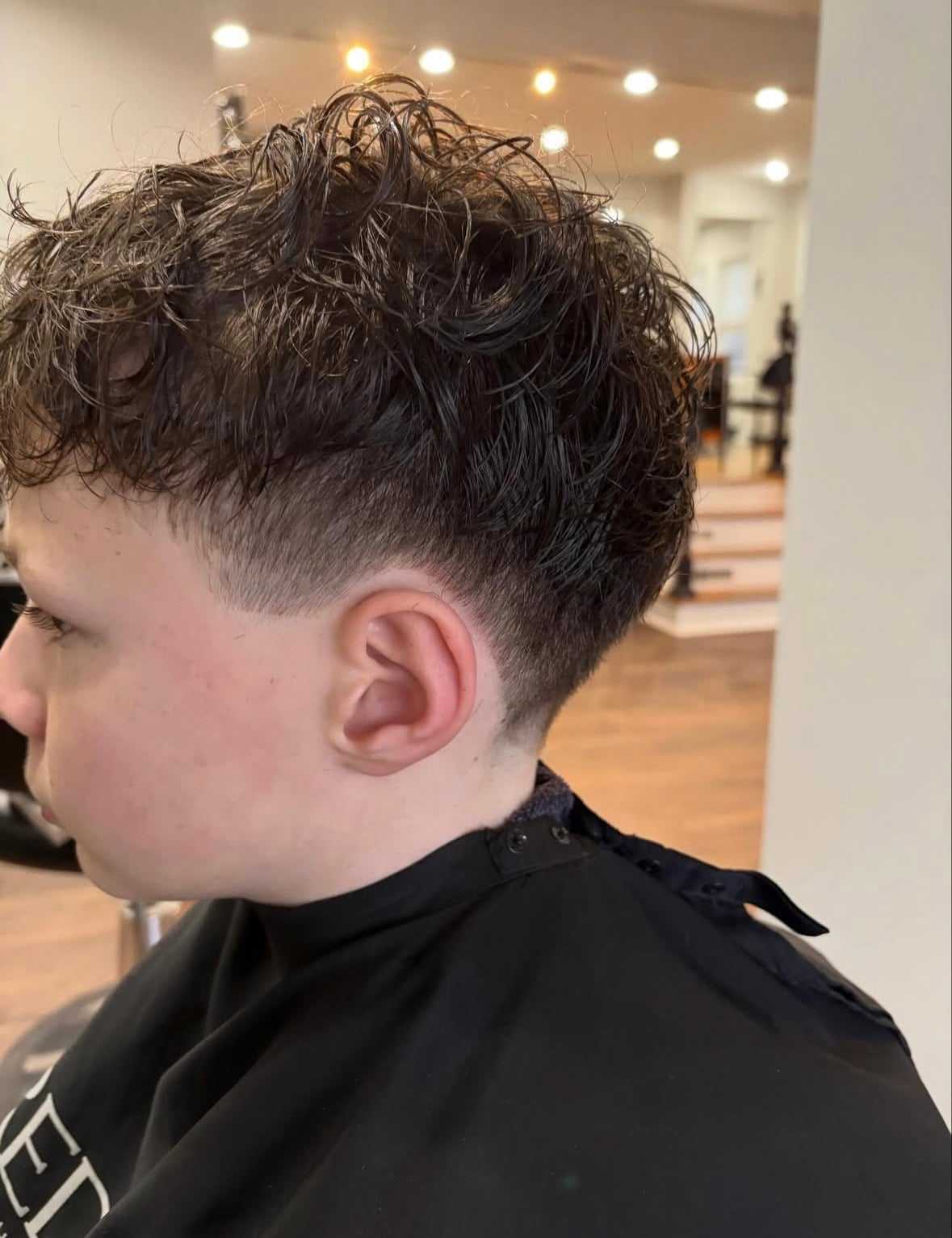 Young person with a short, curly haircut sitting in a barber chair. Modern, fresh style.