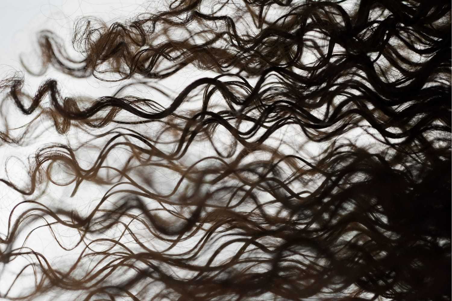Close-up of flowing, curly brown hair against a light background.