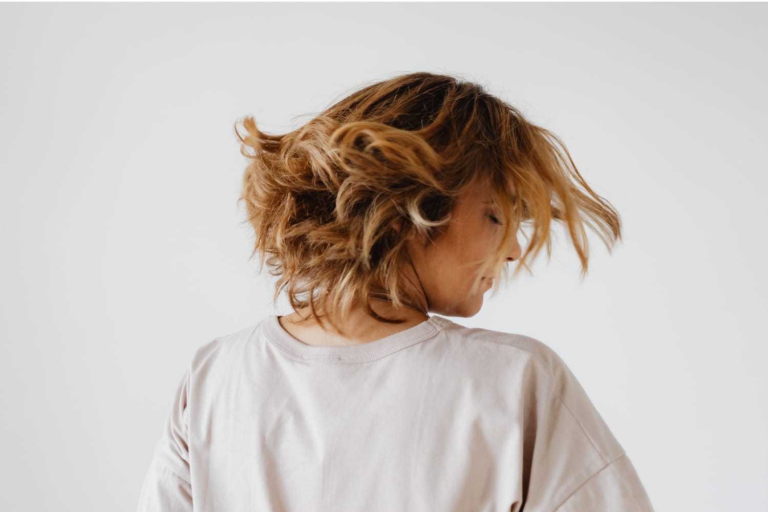 Person with short, tousled hair turning their head, wearing a light pink shirt.