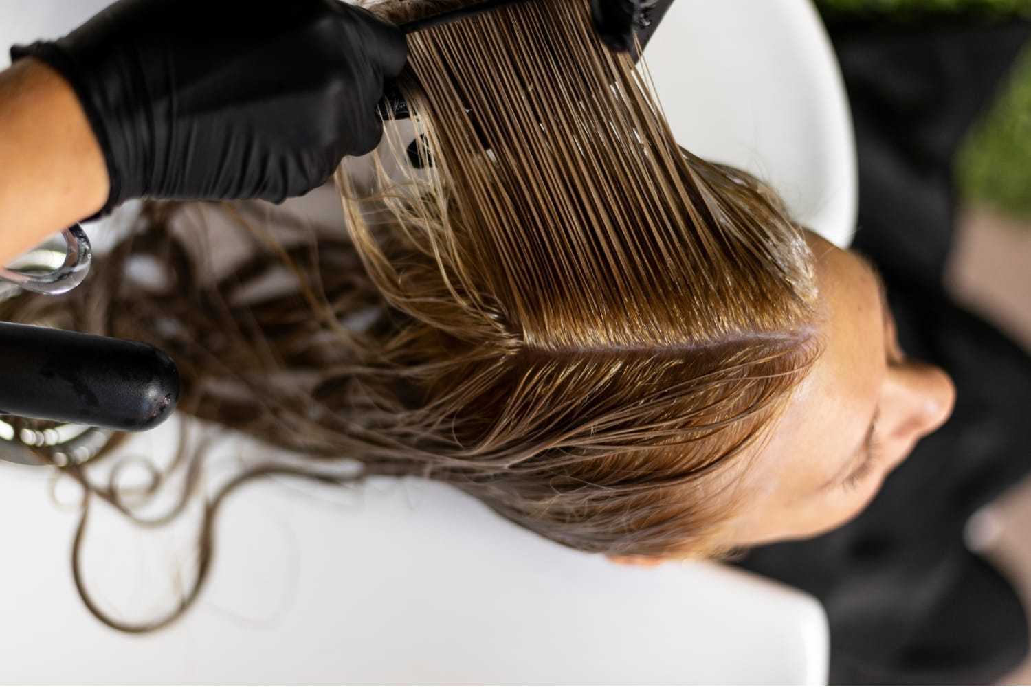 Hairdresser applying color to woman's hair with a brush in a salon.